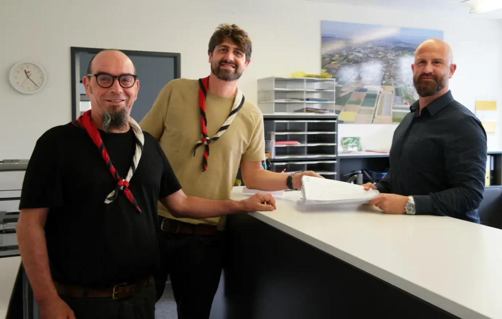 Benno Kohli (Stutz Kohli Architekten) und Benny Kammer (Präsident Altpfadfinder-Stiftung) übergeben die Unterlagen an Gaetano Fiscelli (Abteilungsleiter Baugesuche Gemeinde Wohlen).